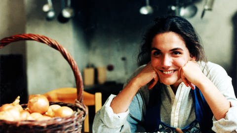 Monique sitzt strahlend am Küchentisch, vor ihr ein Korb mit Zwiebeln (Foto: SWR)