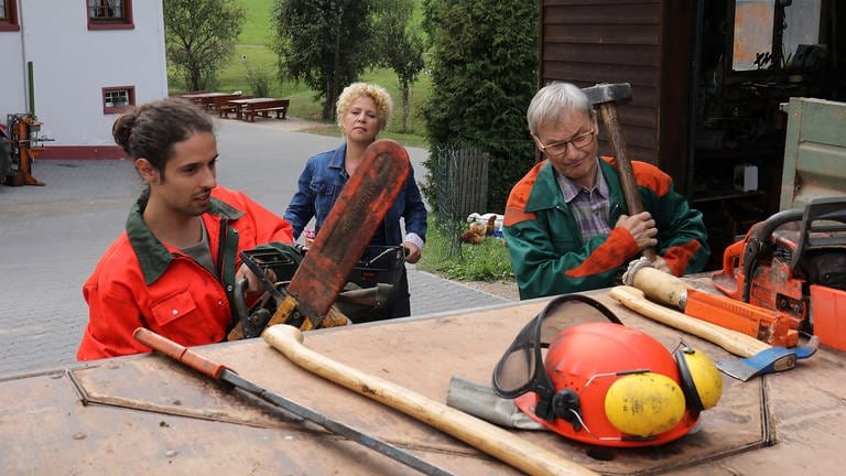 Karl und Albert richten ihr Werkzeug für die Waldarbeit, Bea im Hintergrund (Foto: SWR, Johannes Krieg)