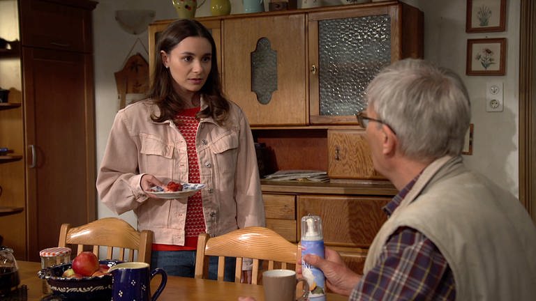 Jenny hält einen Teller mit Obstkuchen und steht vor Karl, der eine Dose Sprühsahne hält und am Küchentisch sitzt (Foto: SWR)
