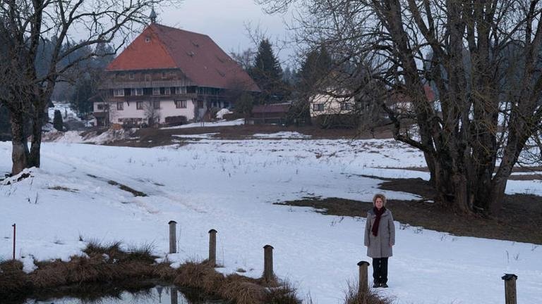 Bea steht auf schneebedeckter Wiese am Weiher, im Hintergrund der Fallerhof (Foto: SWR, SWR/Stephanie Schweigert -)