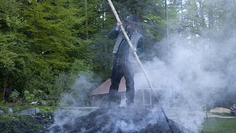 Toni steht auf dem dampfenden Kohlenmeiler und bearbeitet ihn mit einer langen Holzstange (Foto: SWR, SWR/Peter Sebera -)
