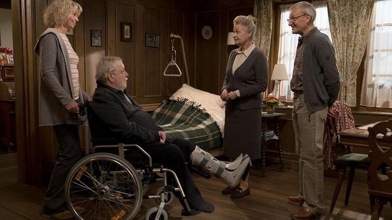 Kati schiebt Hermann, der im Rollstuhl sitzt ins Wohnzimmer, wo Johanna und Karl bereits auf ihn warten (Foto: SWR, SWR/Stephanie Schweigert -)