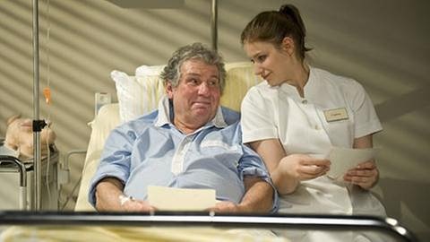 Leo liegt im Krankenbett, Krankenschwester Celine sitzt bei ihm auf der Bettkante (Foto: SWR, SWR/Stephanie Schweigert -)