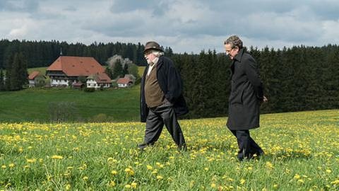 Hermann und Bernhard gehen über eine Frühlingswiese, im Hintergrund der Fallerhof (Foto: SWR, SWR/Stephanie Schweigert -)