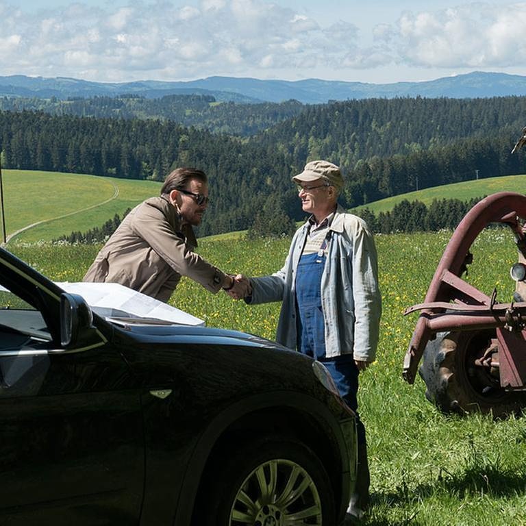 Constantin und Karl begrüßen sich auf freiem Feld, im Vordergrund Constantins Limousine, daneben Karls Traktor (Foto: SWR, SWR/Stephanie Schweigert -)