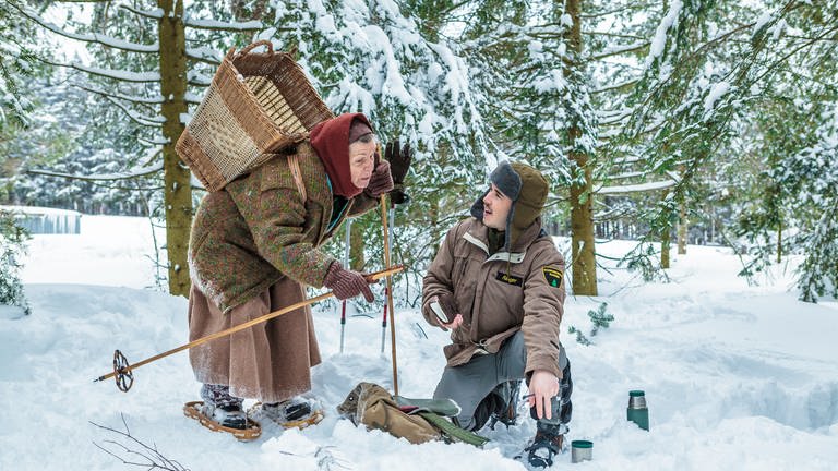 Sebastian kniet im Schnee, Lioba steht neben ihm, sie trägt einen Weidekorb auf dem Rücken (Foto: SWR, Peter Sebera)
