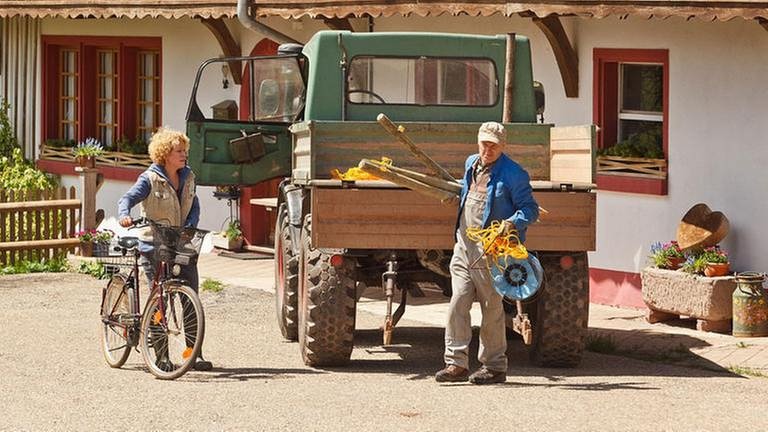 Bea mit dem Fahrrad vor dem Fallerhof, wo Karl gerade Baumaterial vom Unimog lädt (Foto: SWR, SWR/Peter Sebera -)