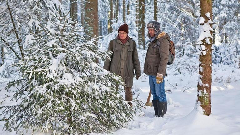 Karl und Andreas im tief verschneiten Wald auf der Suche nach dem perfekten Baum