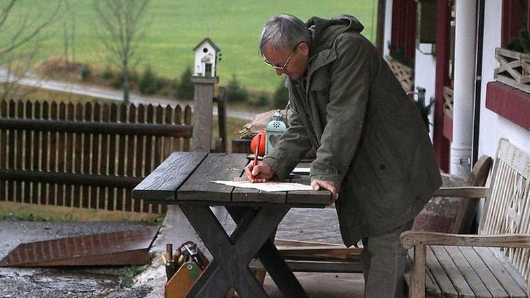 Karl steht am Tisch vor dem Fallerhof und schreibt etwas auf (Foto: SWR, SWR/Johannes Krieg -)
