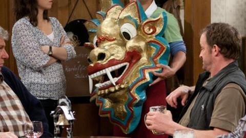 Tu zeigt Eva und den Stammtischjungs eine goldene Drachenmaske (Foto: SWR, SWR/Martin Furch -)