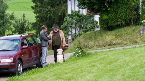 Andreas steht an sein Auto gelehnt neben Hermann, beide schauen auf den Hund Willy herunter (Foto: SWR, SWR/Stephanie Schweigert -)