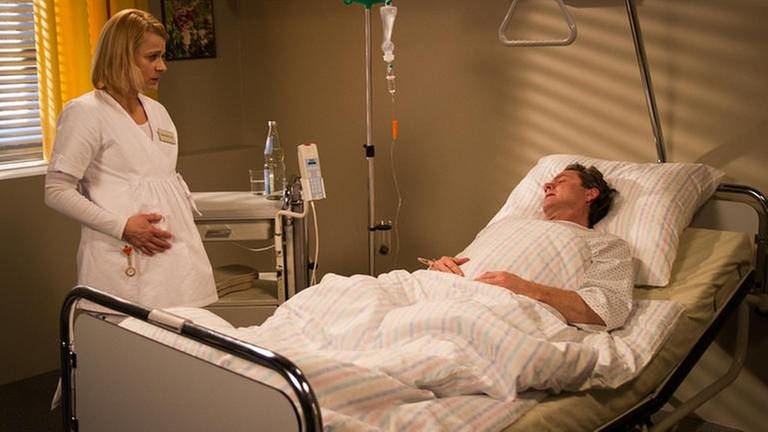 Bernhard liegt im Krankenhaus, Caro steht neben seinem Bett (Foto: SWR, SWR/Michael Cziesielski -)