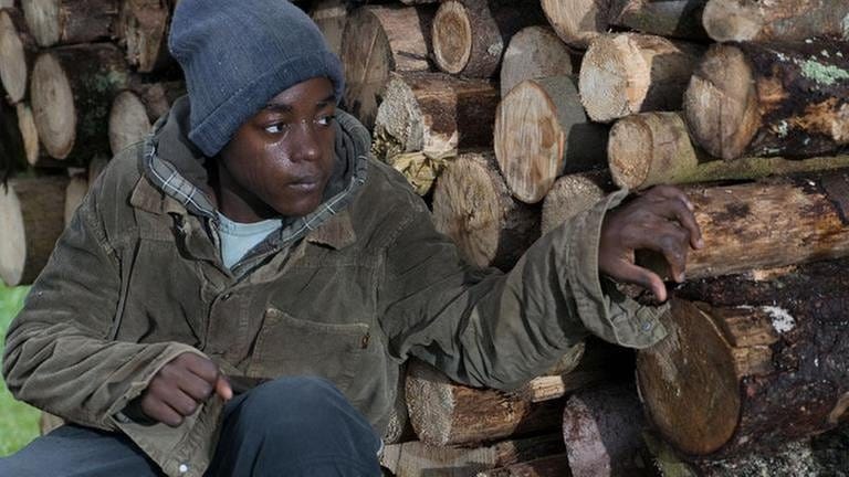 Tayo, der Flüchtlingsjunge, versteckt sich hinter einem Holzstapel (Foto: SWR, SWR/Stephanie Schweigert -)