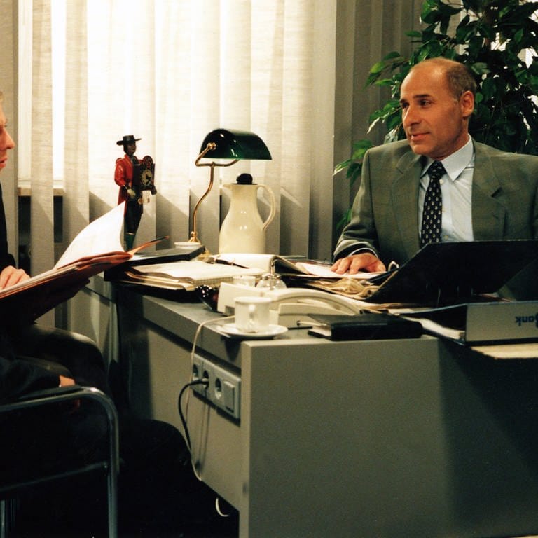 Franz sitzt hinter seinem Schreibtisch, zwei Kunden vor ihm (Foto: SWR)