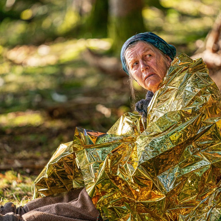Lioba sitzt mit goldener Wärmefolie um die Schultern im Wald