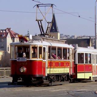 Historischer roter Zug in Prager Altstadt mit Lokführer und mehreren Menschen im Abteil (Foto: SWR)