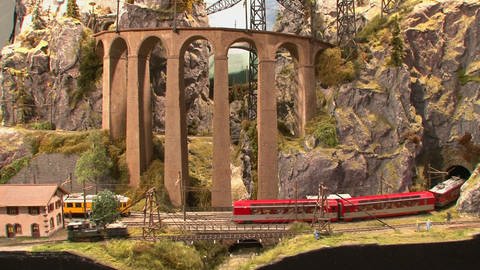 Ein gelber und ein roter Zug einer Modelleisenbahn mit Felsen und Brücke (Foto: SWR)