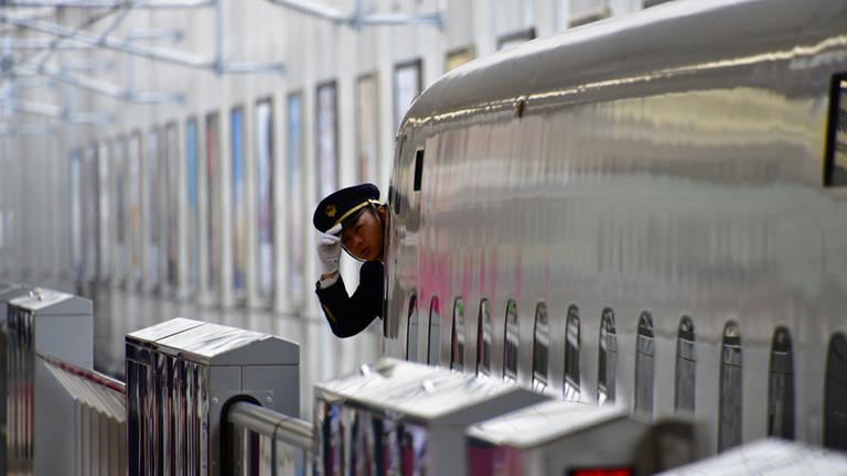 Ein Shinkansen Hochgeschwindigkeitszug fährt aus - der Zugführer schaut aus dem Fenster,  ob alles klar ist. Am Ende des Bahnsteigs hat der Zug bereits eine Geschwindigkeit von rund 120 Kilometer pro Stunde - da muss man die Mütze festhalten.