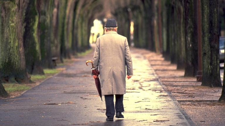 Ein älterer Herr mit einem Regenschirm läuft an einem Herbsttag alleine auf dem Gehweg. (Foto: Colourbox, Foto: Colourbox.de -)