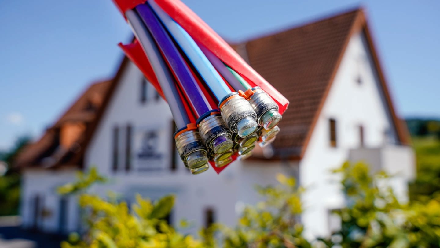 Ein Bündel mit Umhüllungen für Glasfaserkabel hängt an einem Schild und vor einem Wohnhaus. (Foto: dpa Bildfunk, picture alliance/dpa | Uwe Anspach)