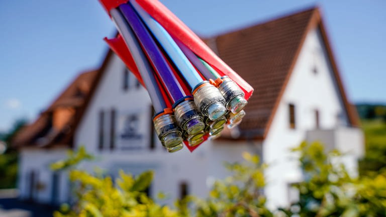 Ein Bündel mit Umhüllungen für Glasfaserkabel hängt an einem Schild und vor einem Wohnhaus.  (Foto: dpa Bildfunk, picture alliance/dpa | Uwe Anspach)