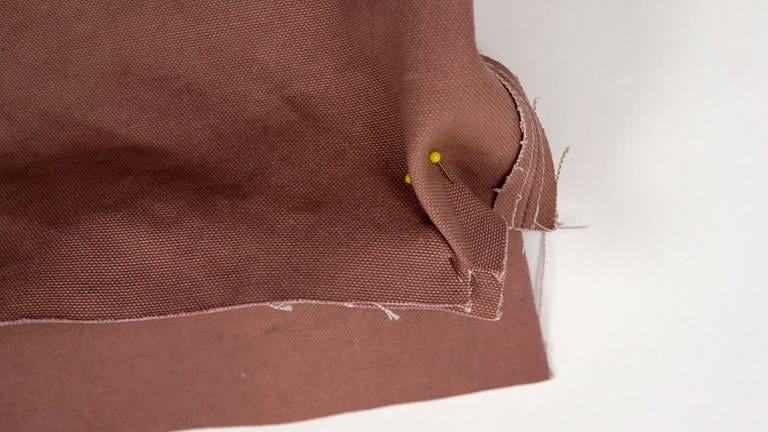Den Boden r-a-r von der Taschenseite aus festnähen: dafür eine Seite des Taschenteils wie beschrieben kantenbündig bis von Knips zu Knips heften.  (Foto: Laura Wilhelm)