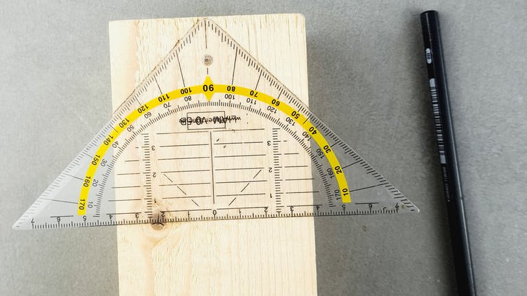 Ein Kantholz nehmen, das Geodreieck mittig auflegen und das Hausdach im 45 Grad Winkel vorzeichnen. (Foto: Lisa Vöhringer)