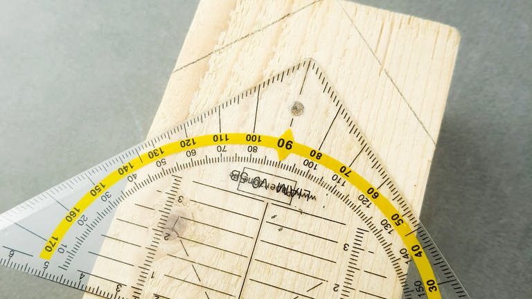 Ein Kantholz mit den Maßen ca. 8x5,5cm nehmen. Das Geodreieck mittig auflegen und das Hausdach im 45 Grad Winkel vorzeichnen.  (Foto: Lisa Vöhringer)