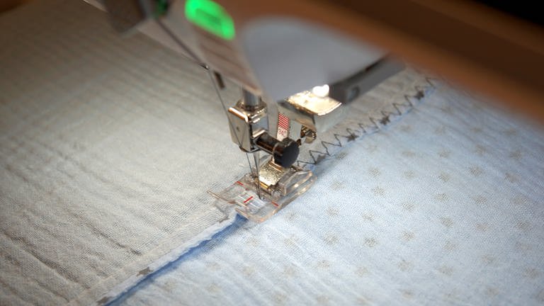 An der Nähmaschine den Dreistich-Zickzackstich oder einen breiten Zierstich einstellen. Die Nahtzugaben mittig von links feststeppen.  (Foto: Laura Wilhelm)