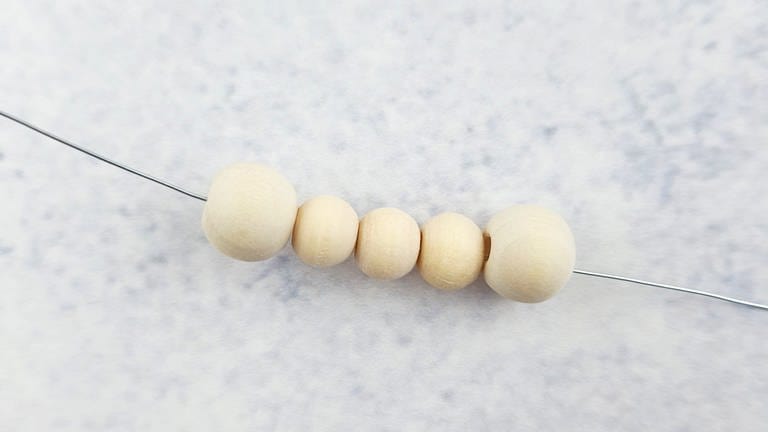 Die lange Drahtseite durch die erste große Perle ziehen und eine große, dann drei kleine und dann erneut eine große Perle (insgesamt 5 Perlen) auf den Draht auffädeln. (Foto: Lisa Vöhringer)
