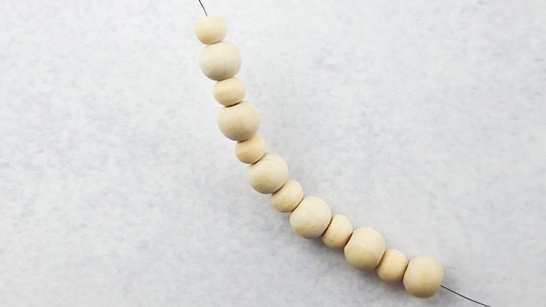 Abwechselnd eine große und eine kleine Holzperle auffädeln, bis 12 Perlen aufgezogen sind. (Foto: Lisa Vöhringer)