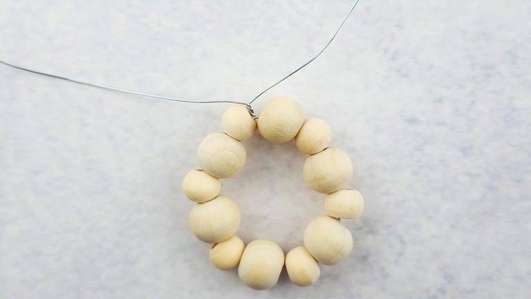 Die aufgezogenen Perlen zu einem Kreis eindrehen und den Draht so miteinander verknoten (Foto: Lisa Vöhringer)
