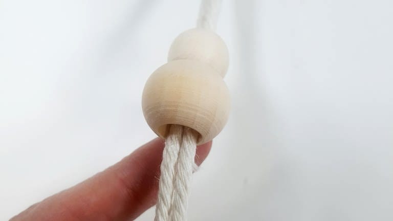 Wer in der Mitte noch ein paar Perlen aufziehen möchte, schneidet nun nochmal 90 cm zu, zieht die Schnur durch den 5 cm Holzring und zieht die gewünschte Anzahl und Größe an Perlen auf.  (Foto: Lisa Vöhringer)