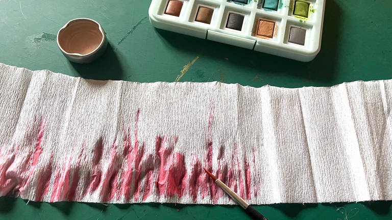 Krepppapierstreifen quer auslegen und die untere Hälfte in Rosé- und Pinktönen bemalen.  (Foto: Karolin Happel)