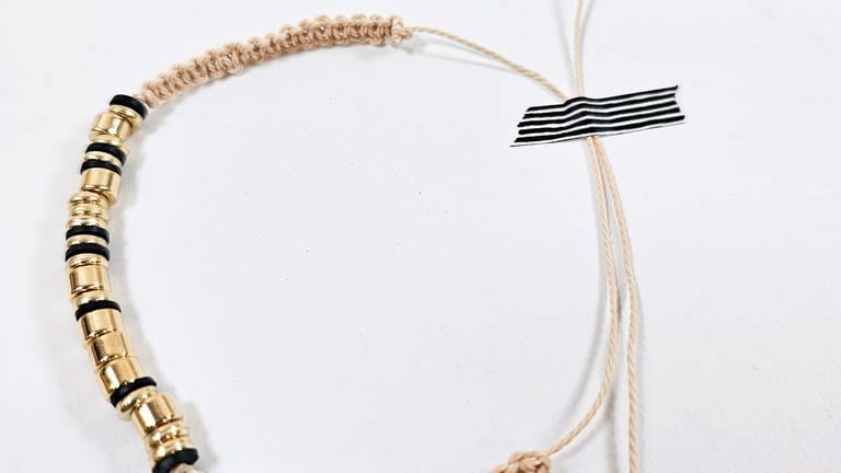 Damit das Armband mit Hilfe eines sogenannten Schiebeverschlusses geöffnet und festgezogen werden kann, werden beide Endschnüre kreisförmig gegeneinander gelegt und mit einem Stück Klebeband fixiert. (Foto: Lisa Vöhringer)