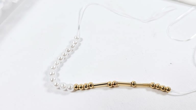 Weitere Perlen (andere Farbe oder Form) rechts und links davon auf das Band aufziehen, bis insgesamt die Länge an Perlen aufgezogen sind, die zum gewünschten Armumfang passen. (Foto: Lisa Vöhringer)