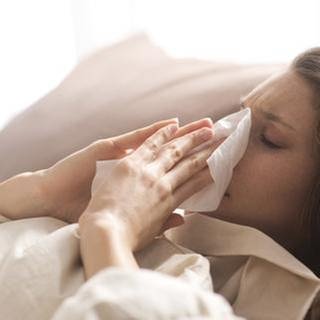 Eine Frau putzt sich die Nase, liegt krank im Bett (Foto: Getty Images, Thinkstock -)