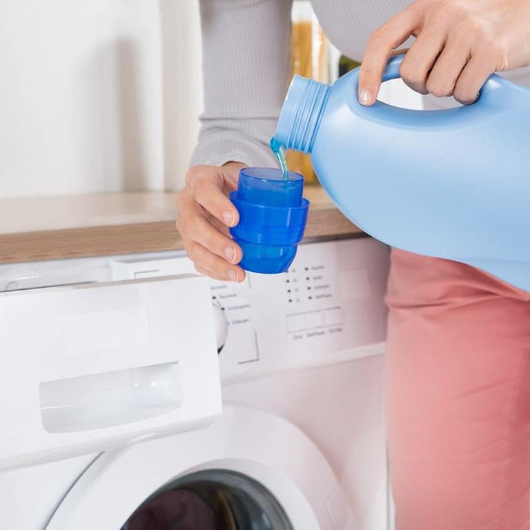 Eine Frau steht vor einer Waschmaschine und gießt Waschmittel in einen Behälter. (Foto: Getty Images, Thinkstock -)