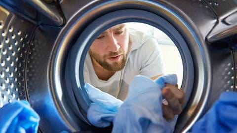 Mann begutachtet kritisch die Wäsche, die er aus seiner Waschtrommel zieht. (Foto: Getty Images, Thinkstock -)