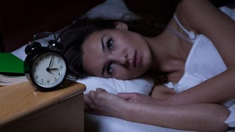 Frau liegt im Bett und schaut auf ihren Wecker der vier nach drei Uhr nachts zeigt. (Foto: Getty Images, Thinkstock -)