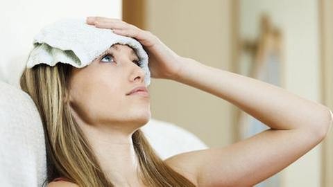 Eine Frau mit Kopfschmerzen legt ein kühles Tuch auf ihre Stirn (Foto: Getty Images, Thinkstock -)