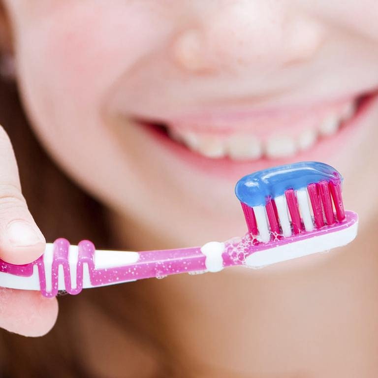 Eine junge frau hält eine Zahnbürste mit Zahnpasta drauf. (Foto: Getty Images, Thinkstock -)