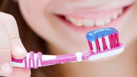 Eine junge frau hält eine Zahnbürste mit Zahnpasta drauf. (Foto: Getty Images, Thinkstock -)