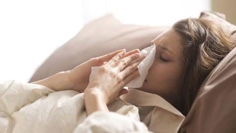Eine Frau putzt sich die Nase, liegt krank im Bett