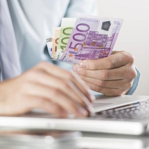 Ein Mann vor einem Laptop hält einige Euroscheine in der Hand (Foto: Getty Images, Thinkstock -)