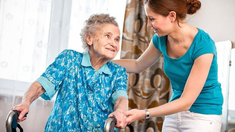 Eine junge Pflegekraft unterstützt eine alte Frau in deren Wohnung. (Foto: Getty Images, Thinkstock -)