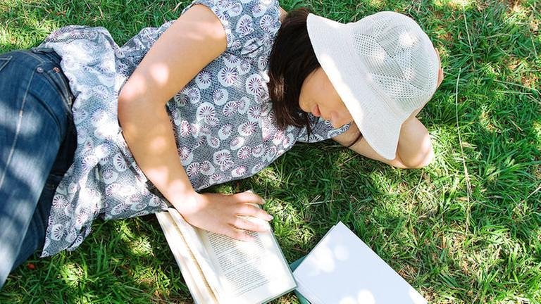 Junge Frau liegt im Schatten unter einem Baum und liest ein Buch. (Foto: Colourbox, Model Foto: Colourbox.de -)