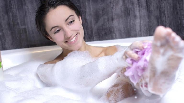 Eine Frau wäscht sich mit einem Schwamm in einer Badewanne voller Schaum.