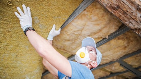 Energie sparen: Mann mit Maske dämmt Dachboden (Foto: Colourbox)