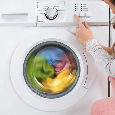 Eine Frau neben einer Waschmaschine. (Foto: Getty Images, Thinkstock -)